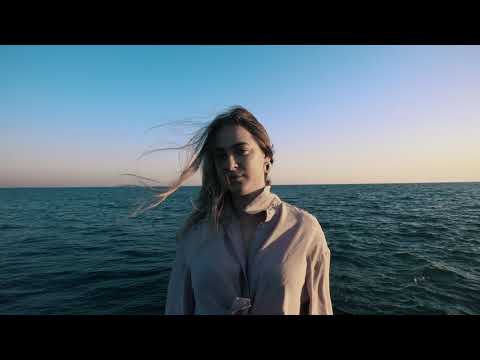 Maria Kravchenko standing on a shoreline in the Broken music video